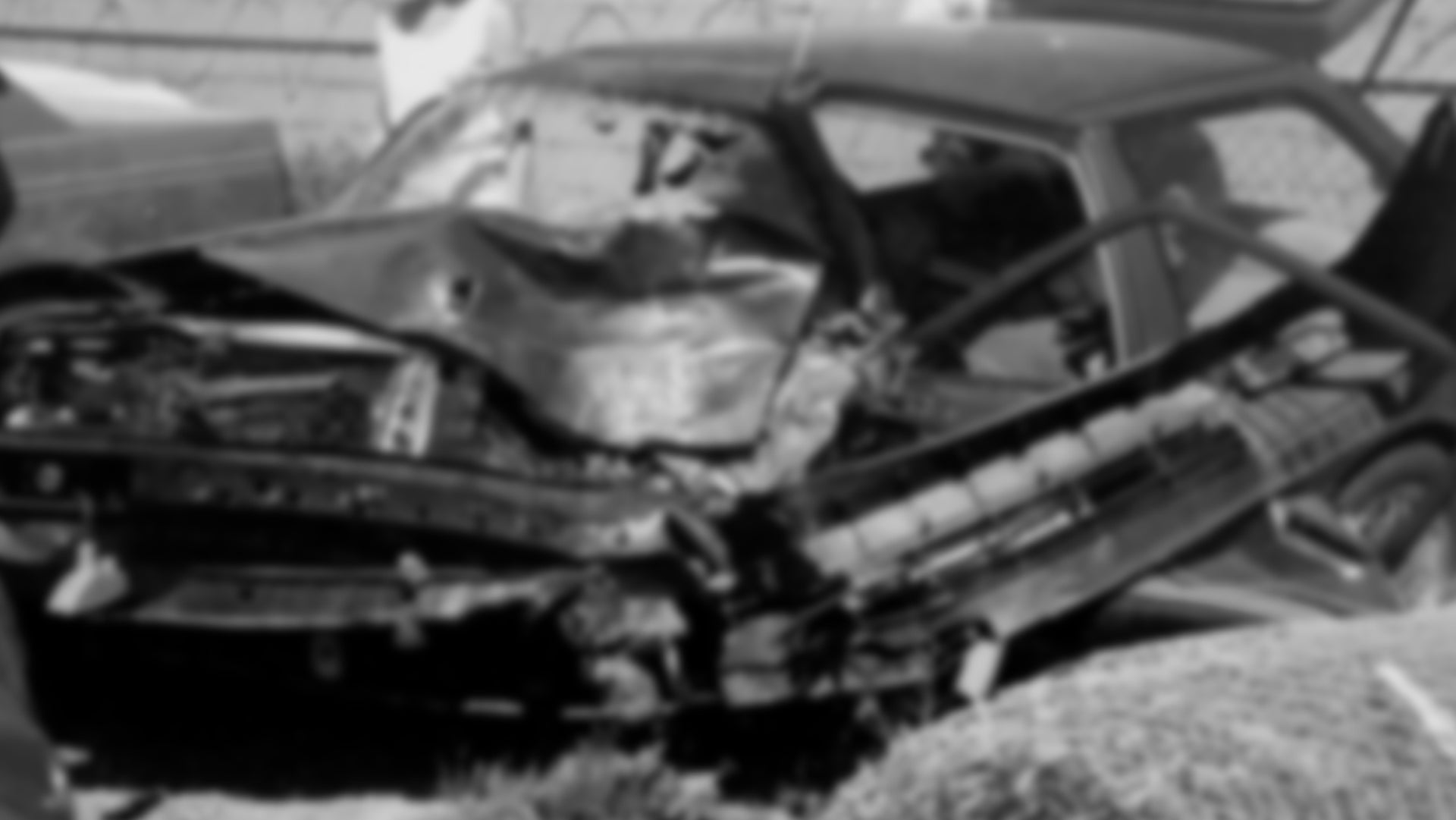 The image appears to show a heavily damaged car from a severe collision, though it has been intentionally blurred. The front end of the vehicle is crushed inward, suggesting a high-impact crash. The blurring obscures specific details, likely for privacy or sensitivity reasons.