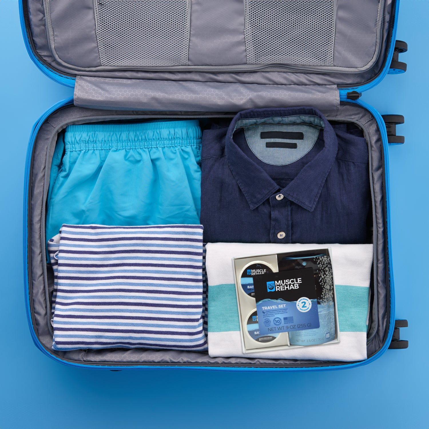 Open suitcase with folded clothes and a Muscle Rehab Gift Set resting on top.